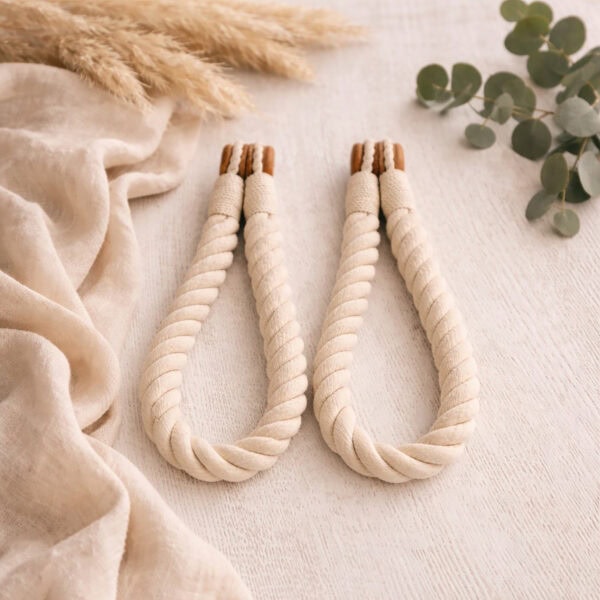 Ecru twisted cotton rope curtain tiebacks with wooden magnetic ends, laid flat on a white surface