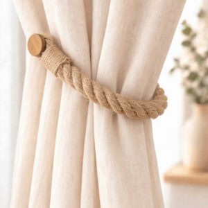 Close-up of a jute twisted rope curtain tieback with a round wooden magnetic end, wrapped around a gathered linen curtain.