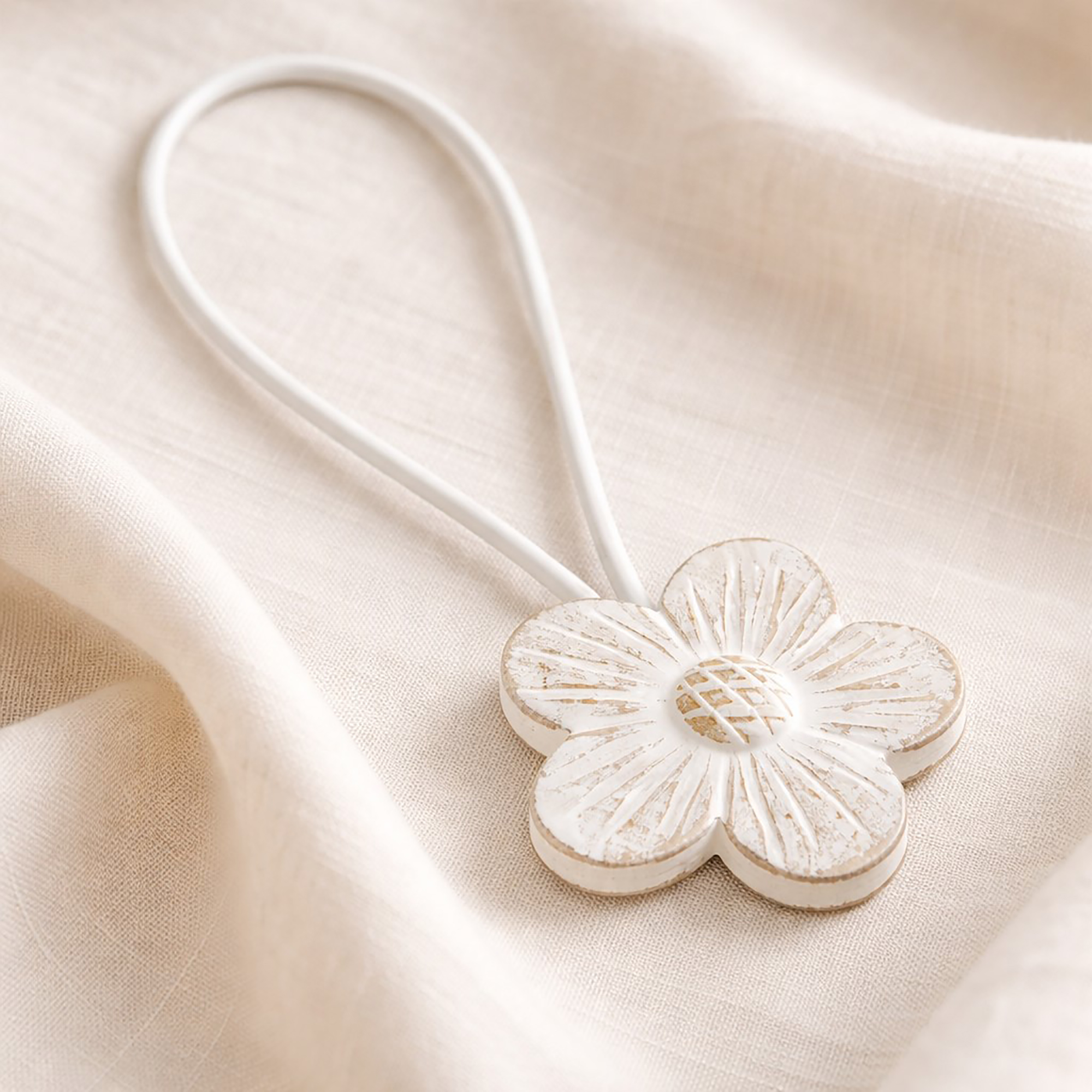White carved resin flower curtain tieback with white cord on linen fabric