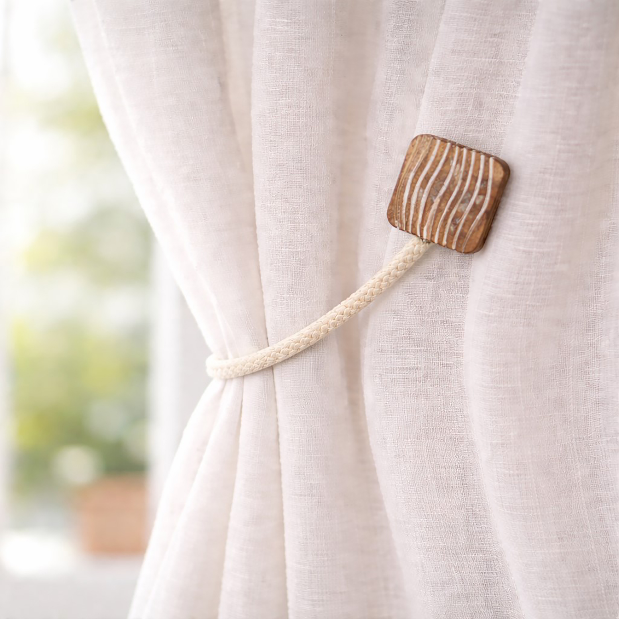 Wood and rope curtain tieback holding sheer curtain panel