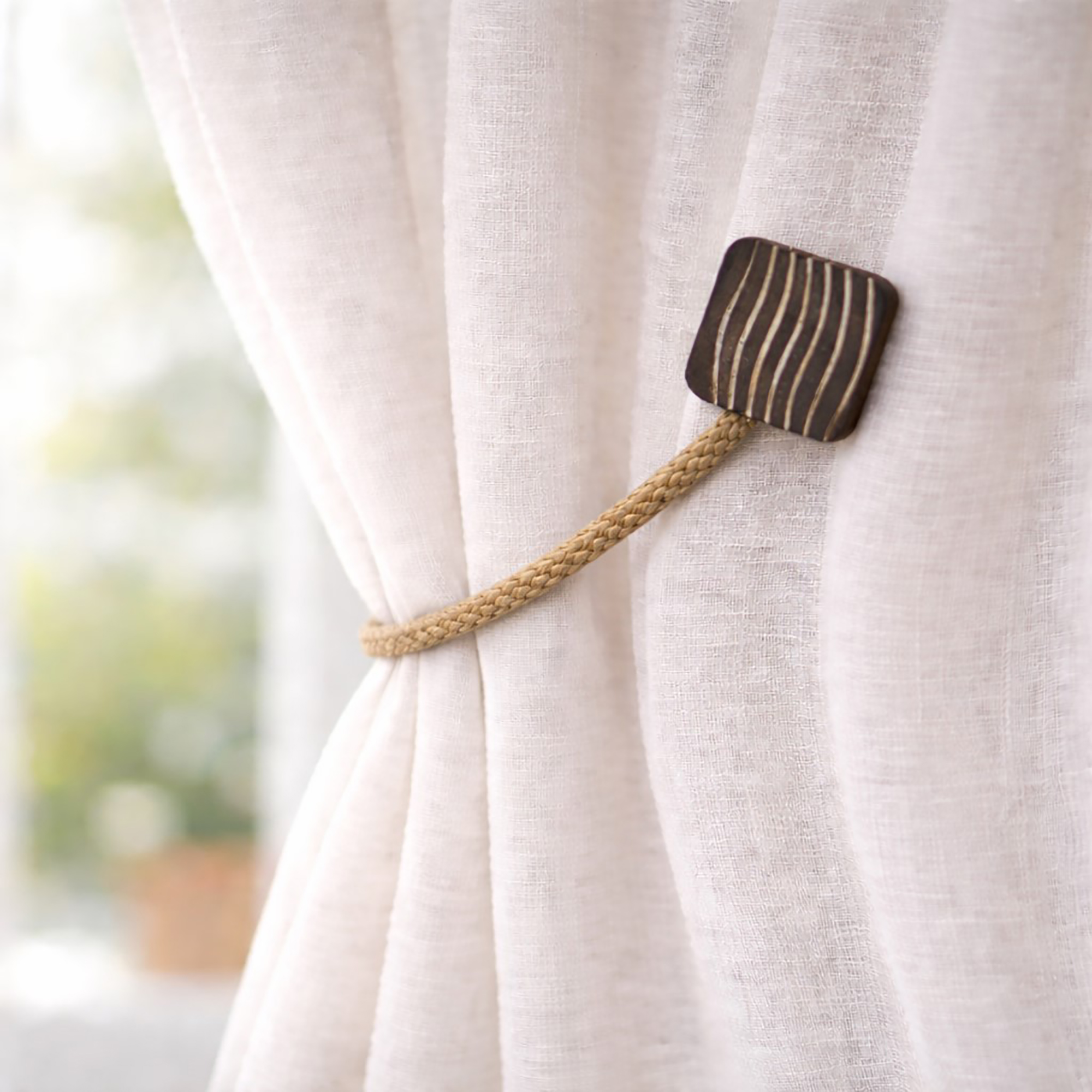 Wood and rope curtain tieback holding sheer curtain panel