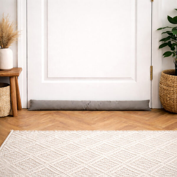 Taupe draft stopper along a white door in a bright entryway with herringbone wood flooring and a woven rug.