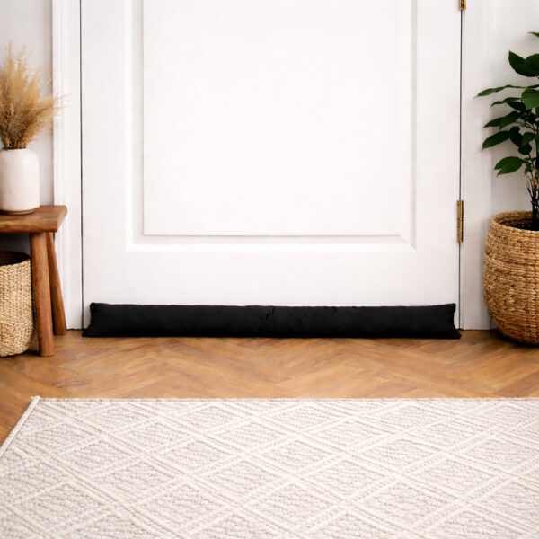 Black draft stopper along a white door in a bright entryway with herringbone wood flooring and a woven rug.