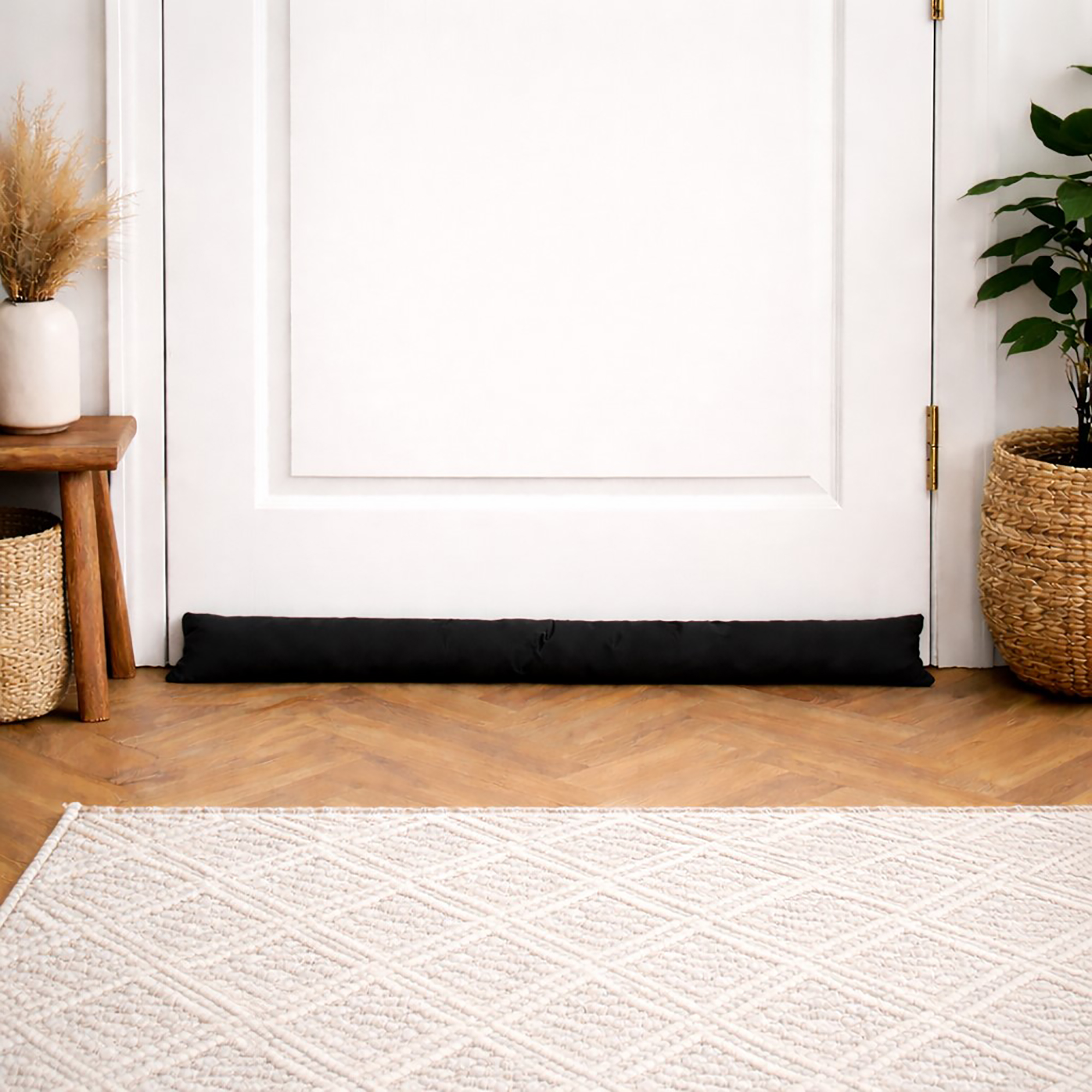 Black draft stopper along a white door in a bright entryway with herringbone wood flooring and a woven rug.