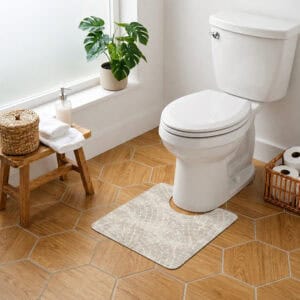 Mosaic Stone contour mat styled around toilet in bright bathroom with monstera plant and wood-look hexagonal tile floor