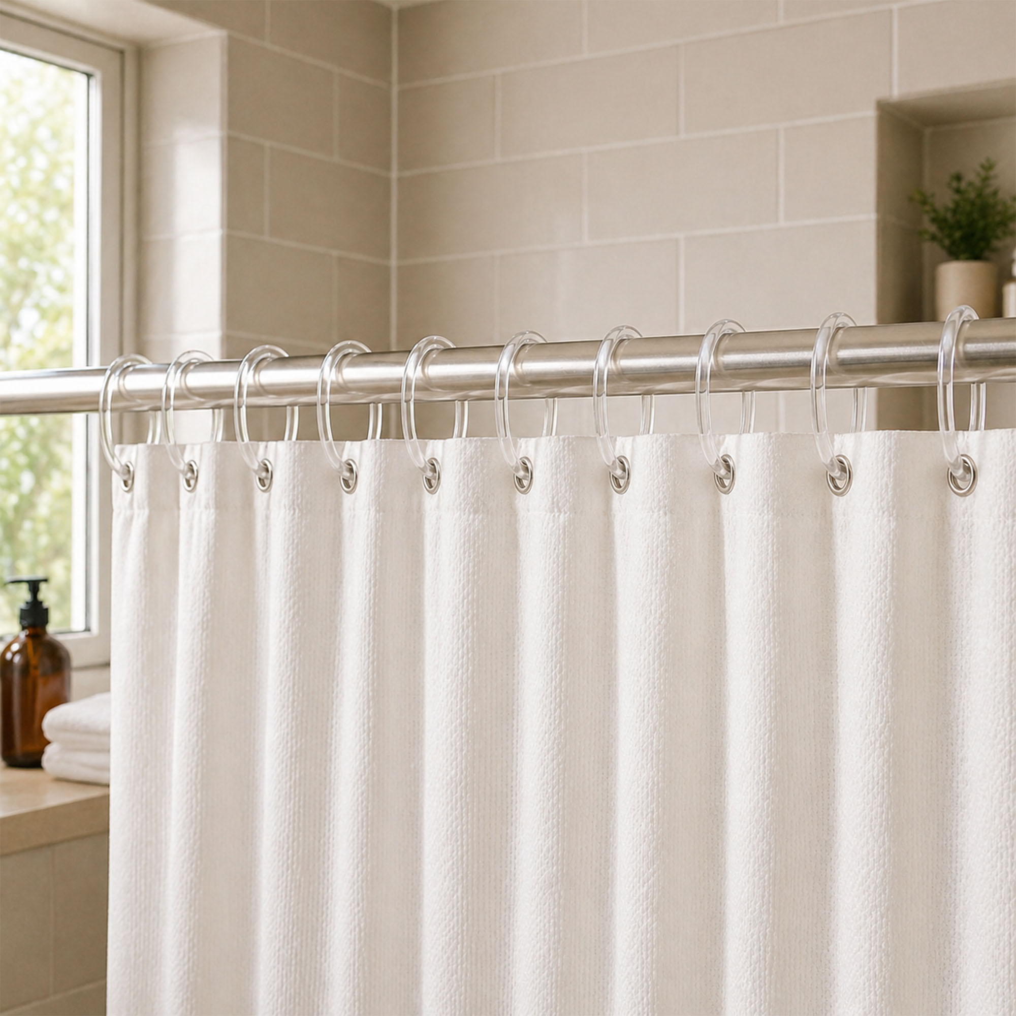 Clear shower curtain rings holding white curtain in bright bathroom with tiled wall and window light