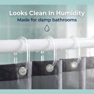 Clear plastic hooks with water droplets on rod holding dark curtain in humid bathroom setting
