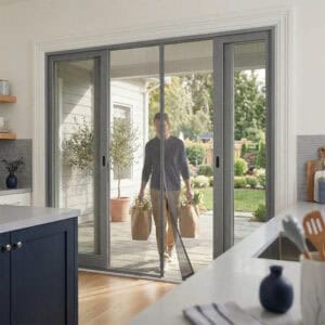 Man carrying grocery bags walking through magnetic screen door on sliding patio doors, hands free entry into modern kitchen with wide 118 inch opening