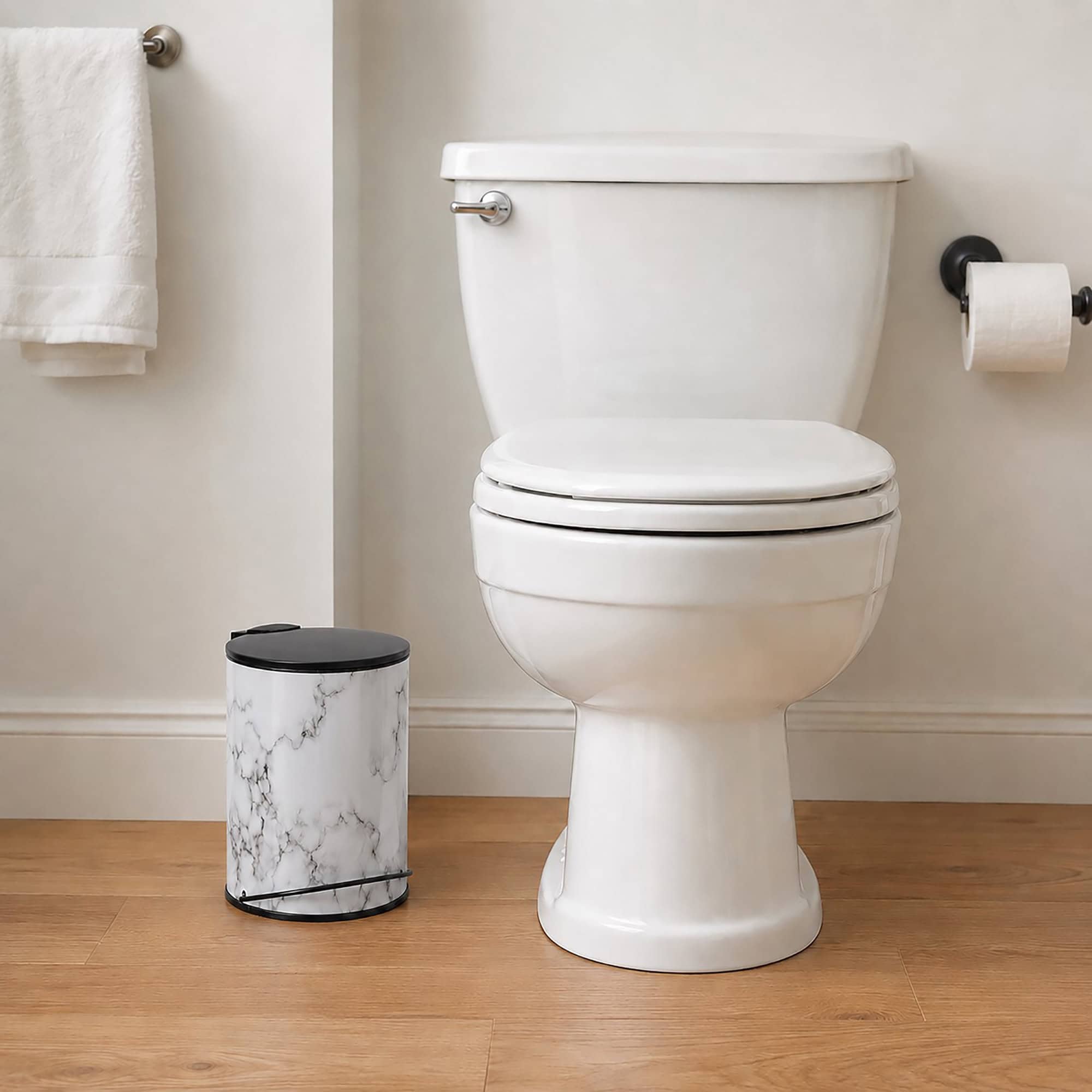Small marble look bathroom trash can with black lid and pedal standing on wood floor next to a white toilet, slim profile for narrow spaces.