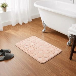 Blush pink rectangular bath mat placed in front of a clawfoot bathtub on warm honey wood flooring, classic chic bathroom setting, soft plush texture inviting comfort