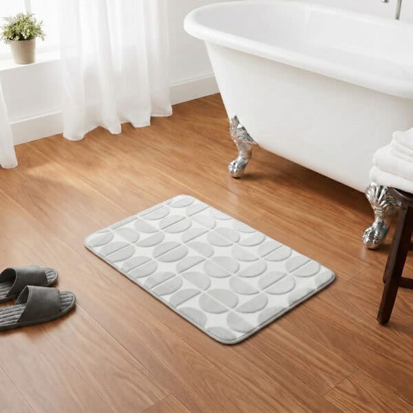 Light gray rectangular bath mat placed in front of a clawfoot bathtub on warm honey wood flooring, classic chic bathroom setting, soft plush texture inviting comfort