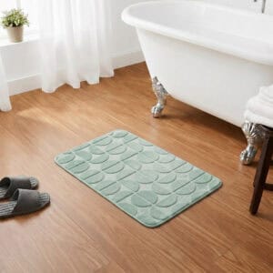 Sage green rectangular bath mat placed in front of a clawfoot bathtub on warm honey wood flooring, classic chic bathroom setting, soft plush texture inviting comfort