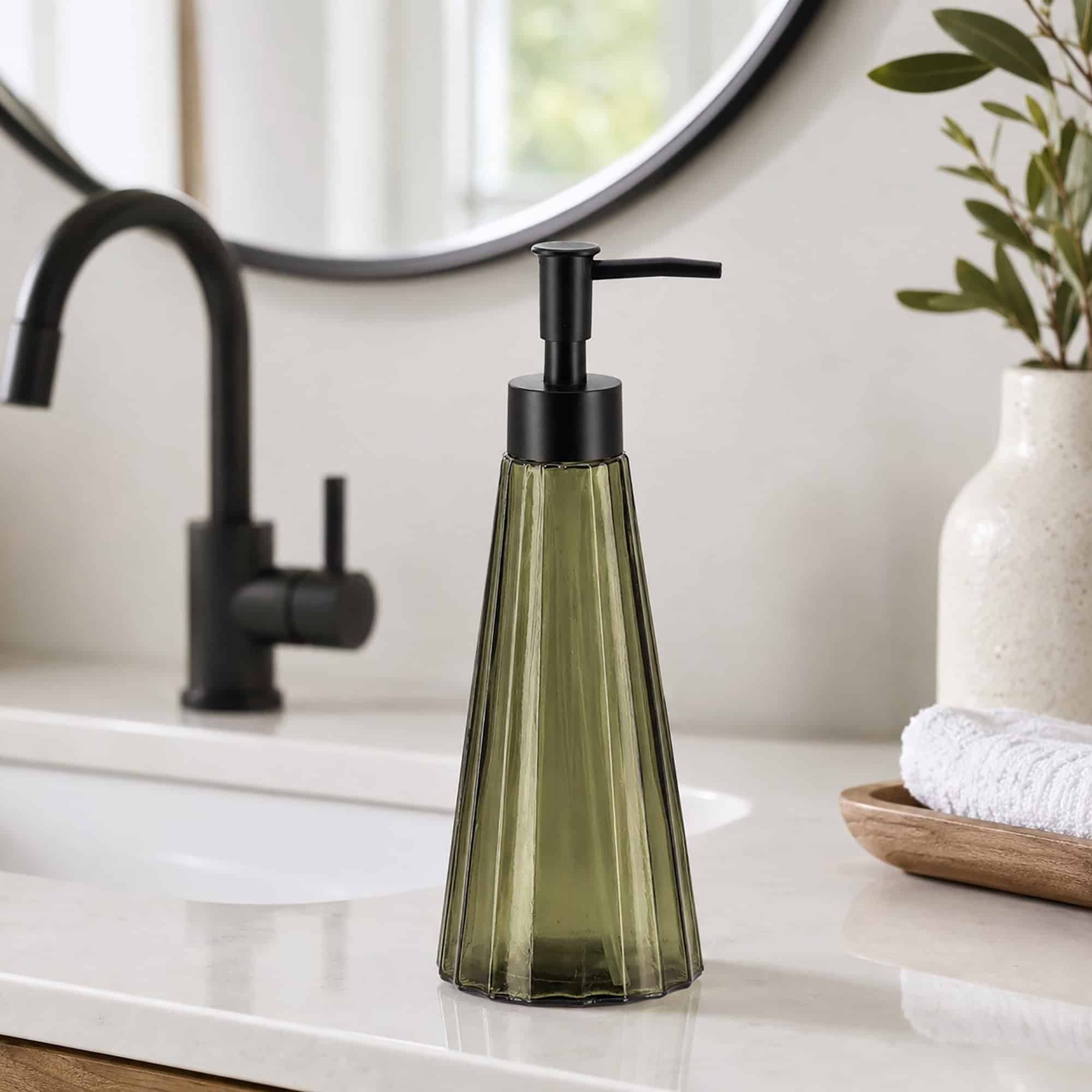 Olive green glass soap dispenser styled on a modern white bathroom vanity with matte black faucet and round mirror