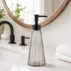 Smoked glass soap dispenser styled on a modern white bathroom vanity with matte black faucet and round wood-framed mirror