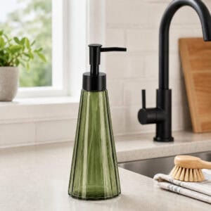 Olive green glass soap dispenser on a light kitchen counter near a matte black gooseneck faucet and natural sponge