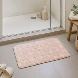 Blush pink plush bath mat at the exit of a walk-in glass shower, modern Scandinavian bathroom with light tile floor and natural daylight, soft landing after every shower