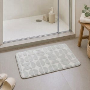 Light gray plush bath mat at the exit of a walk-in glass shower, modern Scandinavian bathroom with light tile floor and natural daylight, soft landing after every shower