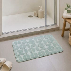 Sage green plush bath mat at the exit of a walk-in glass shower, modern Scandinavian bathroom with light tile floor and natural daylight, soft landing after every shower