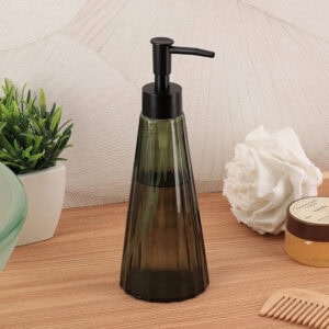 Olive green glass soap dispenser styled with a green plant, white loofah, vanilla body scrub, and bamboo comb on a wood surface