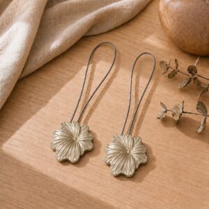 01 (set-of-2 packshot): Set of two matte gold metal flower curtain tiebacks with thin silver cable loops, shown against a plain background to highlight the sculpted petal detail.