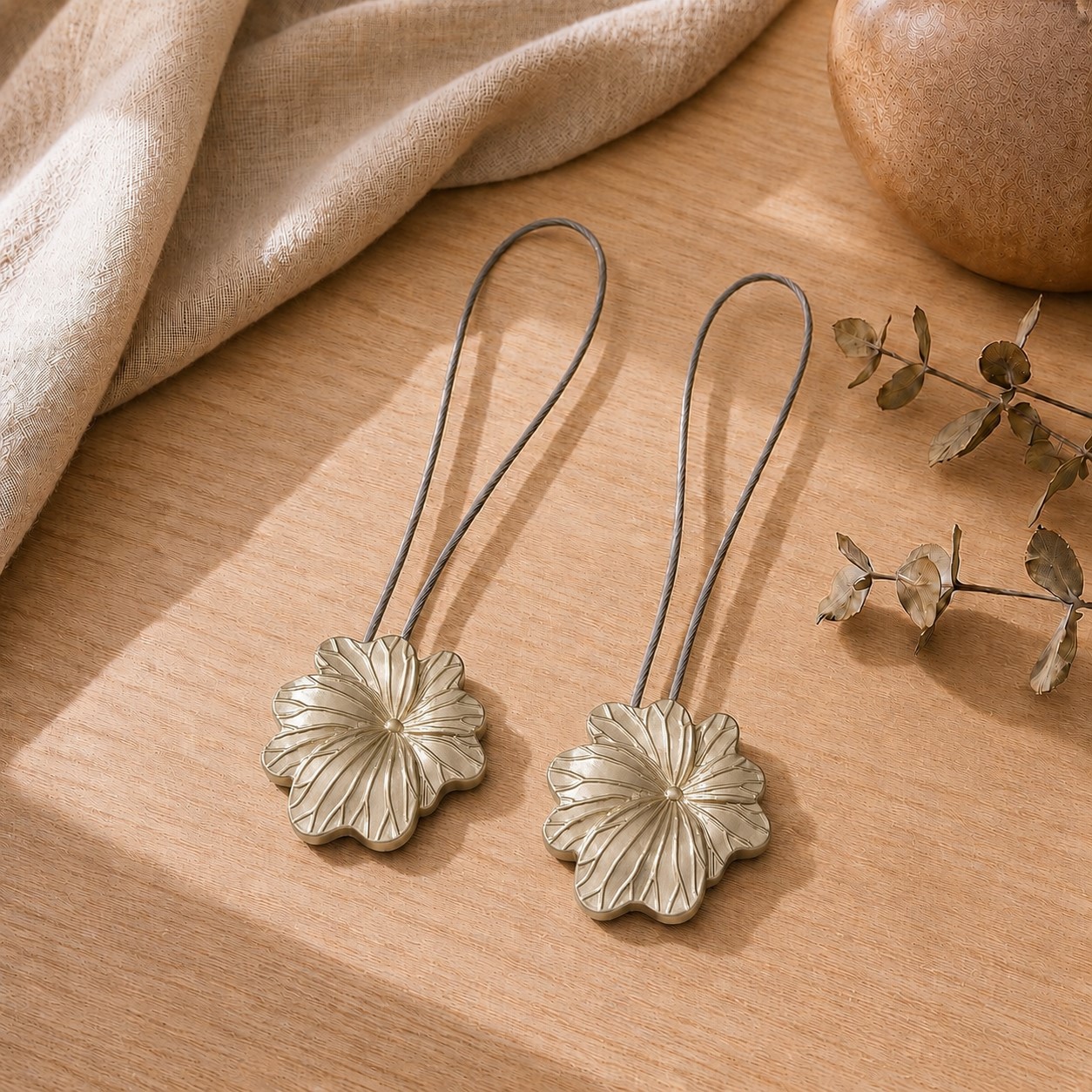 01 (set-of-2 packshot): Set of two matte gold metal flower curtain tiebacks with thin silver cable loops, shown against a plain background to highlight the sculpted petal detail.