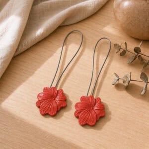 02 (pair, cozy styled): Two terracotta flower tiebacks with looped silver cables resting on a warm wood surface beside soft linen and dried eucalyptus, styled to show the pair in a cozy neutral setting.