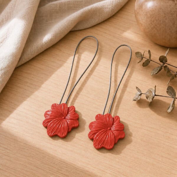 02 (pair, cozy styled): Two terracotta flower tiebacks with looped silver cables resting on a warm wood surface beside soft linen and dried eucalyptus, styled to show the pair in a cozy neutral setting.