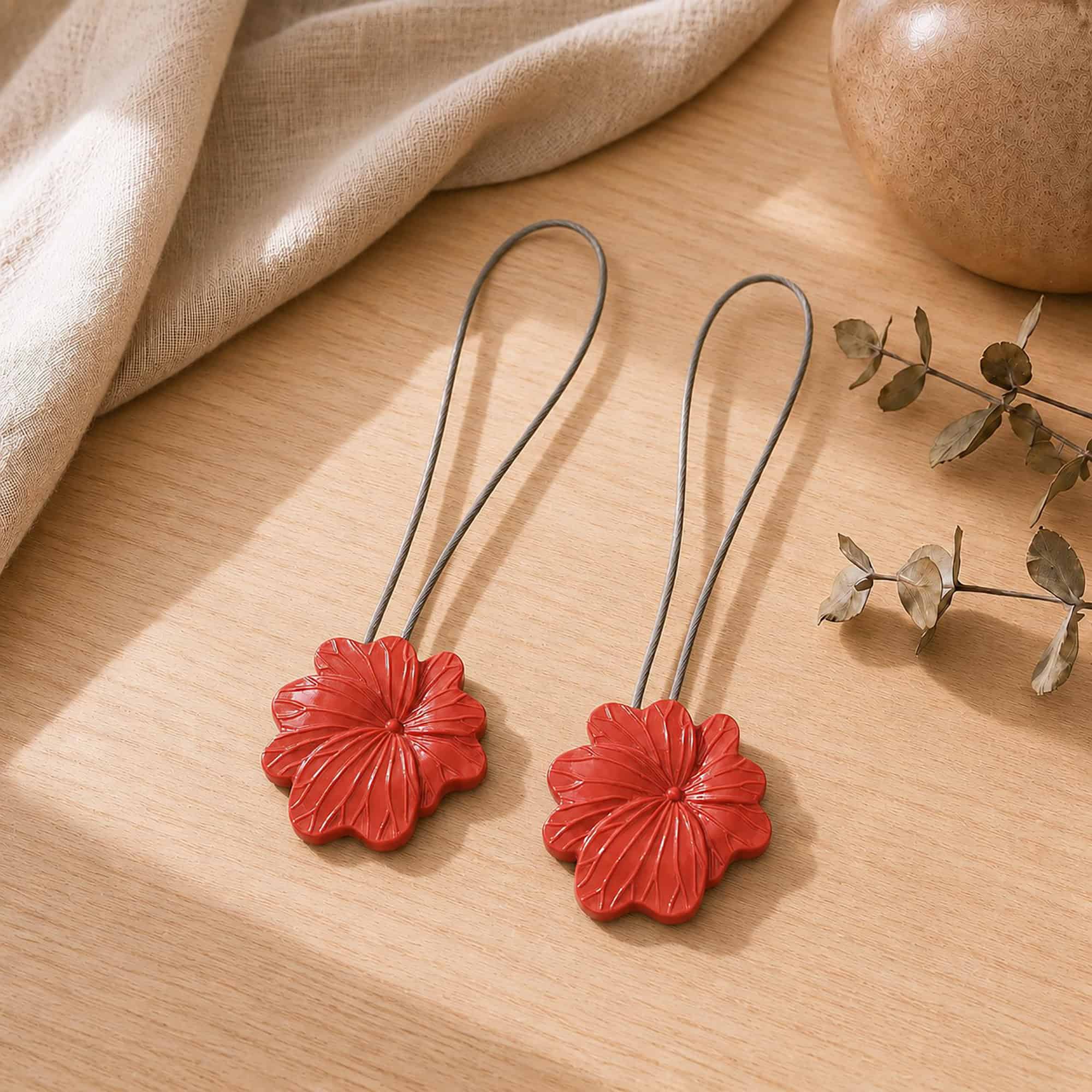 02 (pair, cozy styled): Two terracotta flower tiebacks with looped silver cables resting on a warm wood surface beside soft linen and dried eucalyptus, styled to show the pair in a cozy neutral setting.
