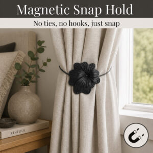 02 (magnetic snap hold): Matte black flower tieback holding a gathered oatmeal linen curtain beside a styled nightstand, its magnetic ends snapping shut with no ties or hooks needed.