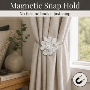 02 (magnetic snap hold): White flower tieback holding a gathered oatmeal linen curtain beside a styled nightstand, its magnetic ends snapping shut with no ties or hooks needed.