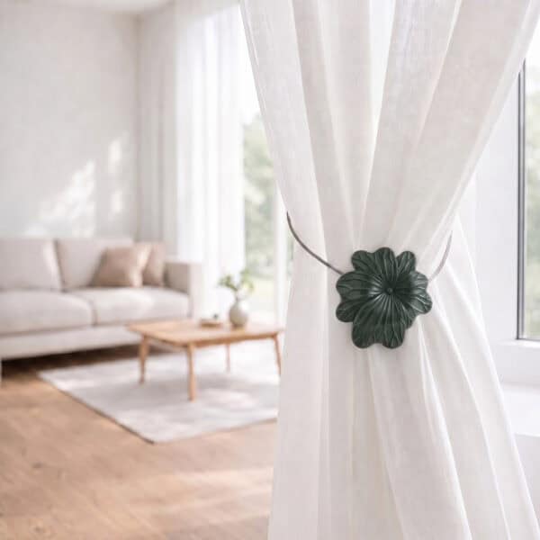 08 (living room lifestyle): Sheer white curtain held back by the khaki flower tieback in a bright living room with a neutral sofa and wood coffee table softly blurred behind.