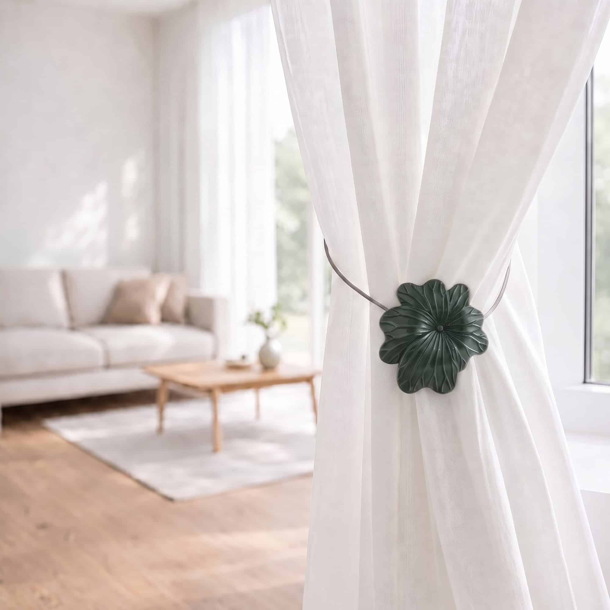 08 (living room lifestyle): Sheer white curtain held back by the khaki flower tieback in a bright living room with a neutral sofa and wood coffee table softly blurred behind.