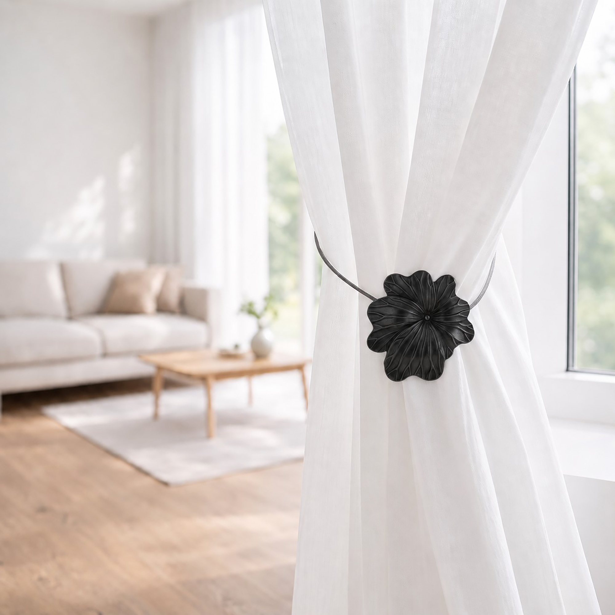 08 (living room lifestyle): Sheer white curtain held back by the matte black flower tieback in a bright living room with a neutral sofa and wood coffee table softly blurred behind.