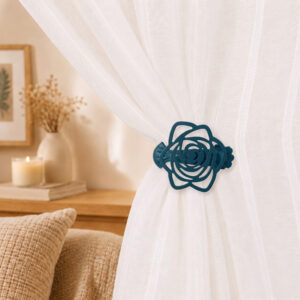 Close-up of a teal blue rose-shaped curtain tieback clip holding a white sheer curtain, styled in a cozy bedroom setting with a lit candle in the background.