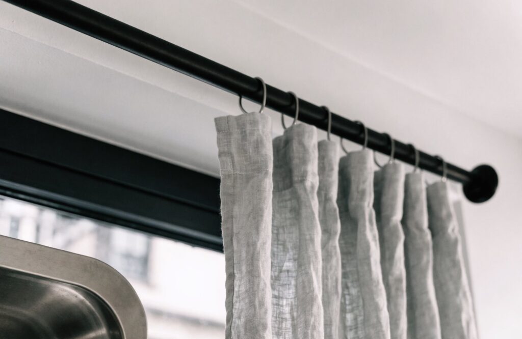 Matte black iron curtain rod with a gray linen curtain on rings above a kitchen window