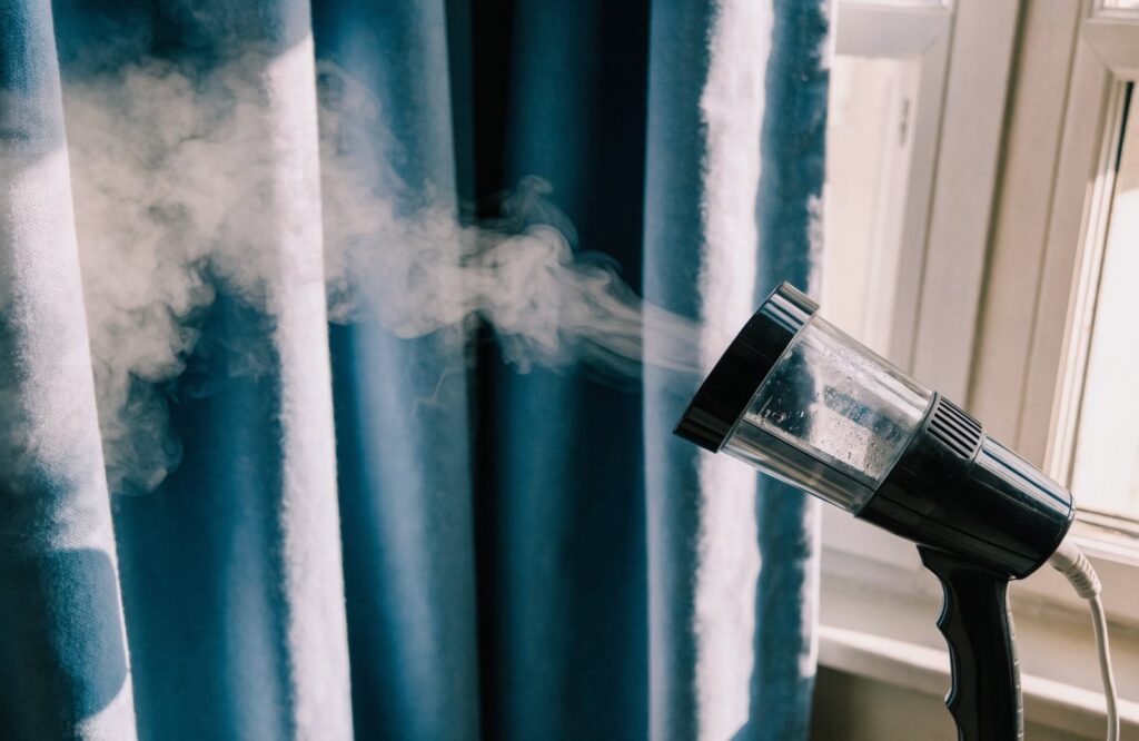 Handheld steamer releasing steam on a heavy blue cotton curtain